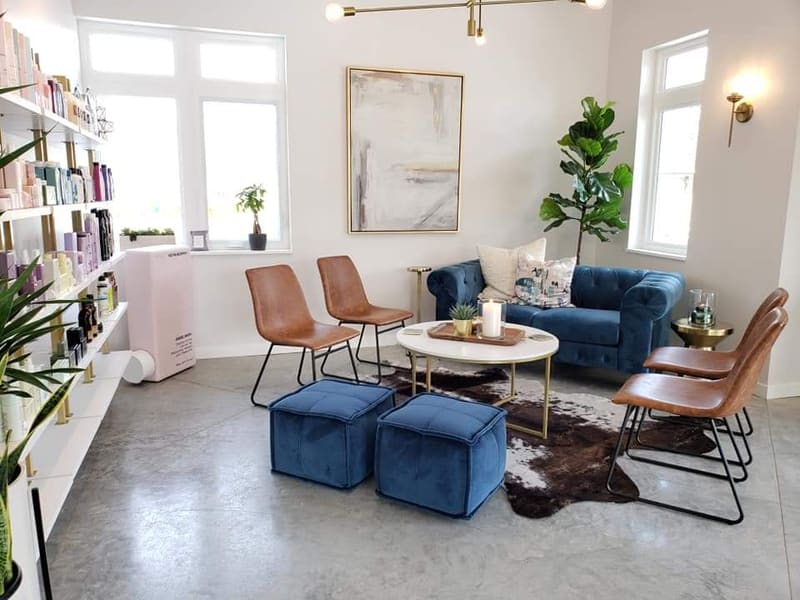 The waiting lounge at AT.hair & co., with a navy velvet chesterfield sofa, cognac leather chairs, and brass accents.