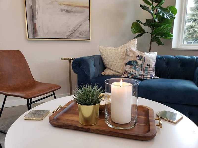 Close view of the lounge at AT.hair & co.: velvet chesterfield with cream pillows, a white round coffee table with a walnut tray, a lit candle, a succulent in a brass pot, and a fiddle-leaf fig.