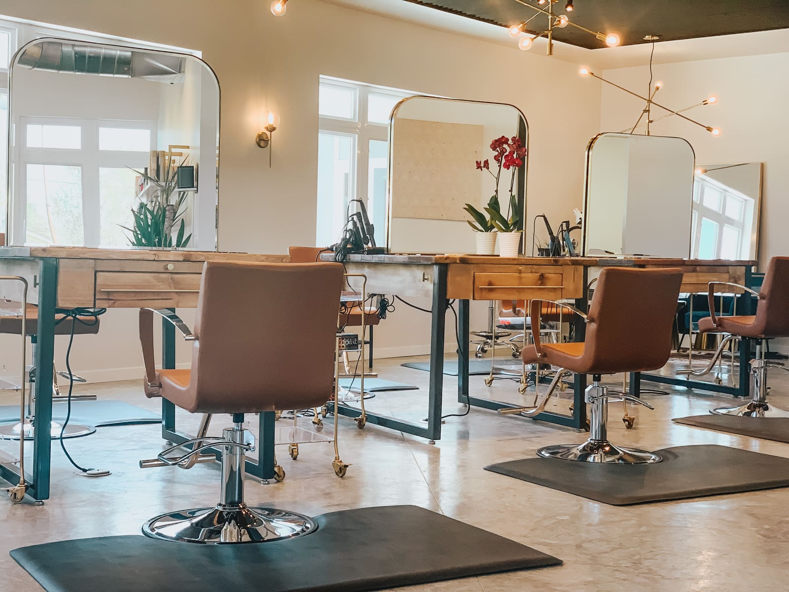 The styling floor at AT.hair & co., with reclaimed-wood stations, arched brass mirrors, and cognac leather chairs in daylight.